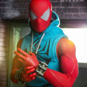 Puede incluir: Una persona con un traje de Spider-Man rojo y negro con una sudadera con capucha azul. El traje tiene un patr&oacute;n texturizado y la persona lleva guantes negros.
