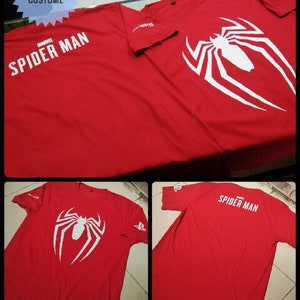 May include: Two red t-shirts with a white Spider-Man logo. One shirt has the text "Marvel Spider-Man" and the other has the text "Spider-Man".