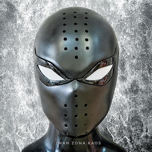 May include: A black full-face mask with numerous small, circular ventilation holes. The eye openings are white with a mesh texture, and the mask has a sleek, metallic appearance. The mask is displayed on a black mannequin head.