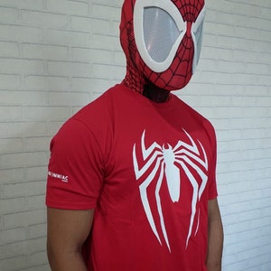 May include: A red t-shirt with a white spider-man logo on the front. The person wearing the shirt is also wearing a red and white spider-man mask.