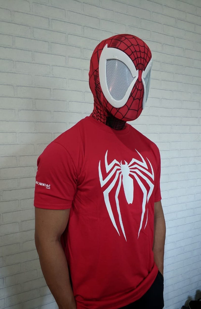 May include: A red t-shirt with a white spider-man logo on the front. The person wearing the shirt is also wearing a red and white spider-man mask.