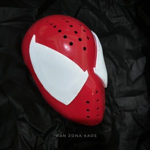 May include: Red and white plastic mask with a spider web design and holes for ventilation. The mask is on a black background. "Iwan Zona Kaos" is written in white text at the bottom of the image.