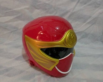 May include: Red plastic helmet with a gold and white design. The helmet has a black visor and a gold symbol on the top.