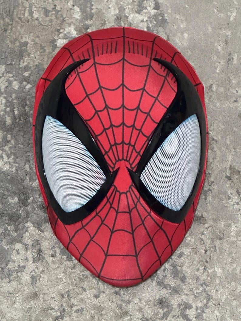 Op de afbeelding: Een rood Spider-Man masker met een zwart webpatroon en zwarte oogomrandingen. De oogopeningen zijn wit met kleine zwarte stippen. Het masker bedekt het hele gezicht.
