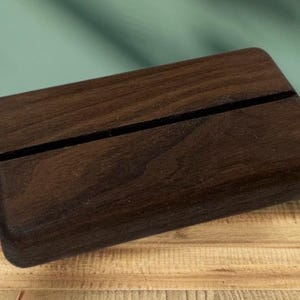 Op de afbeelding: Een donkerbruine houten displaystandaard met een gleuf in het midden om een visitekaartje of ander klein voorwerp in te plaatsen.