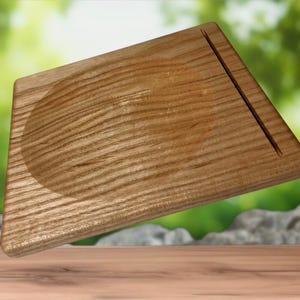 May include: A wooden cutting board with a light brown finish. The board has a rounded indentation on one side and a groove on the other. The wood grain is visible, and the board appears to be new.