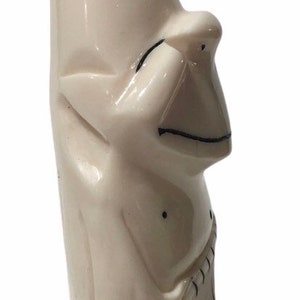 May include: A white carved figurine of a person with a pointed hat and a simple facial expression. The figurine is made of ivory and has black details.