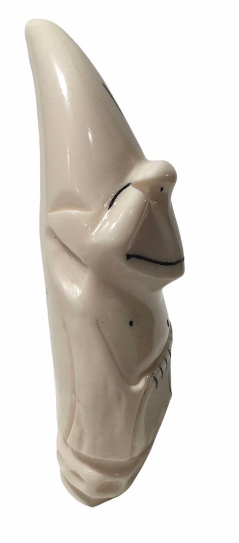 May include: A white carved figurine of a person with a pointed hat and a simple facial expression. The figurine is made of ivory and has black details.