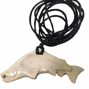 May include: Off-white fish pendant necklace with a black cord. The fish pendant is carved with detailed scales and fins. The cord is knotted at the top of the pendant and is approximately 24 inches long.