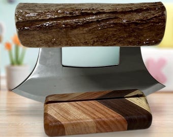 Peut inclure: Un couteau mezzaluna en acier inoxydable avec une poignée en bois et un petit bloc de bois avec un motif en chevrons. La poignée est marron et texturée, ressemblant à une bûche. Le bloc de bois présente des tons de bois clairs et foncés.