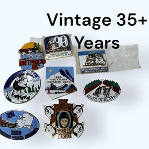 Pode incluir: Uma coleção de pins vintage do Iditarod, apresentando imagens de cães de trenó, paisagens e o texto "Vintage 35+ Years". Os pins são de várias formas e cores, com datas da década de 1980.