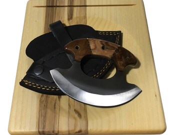 Peut inclure: Un couteau à manche noir avec une lame courbe et un manche en bois posé sur une planche à découper en bois. Le couteau est dans un fourreau en cuir noir.