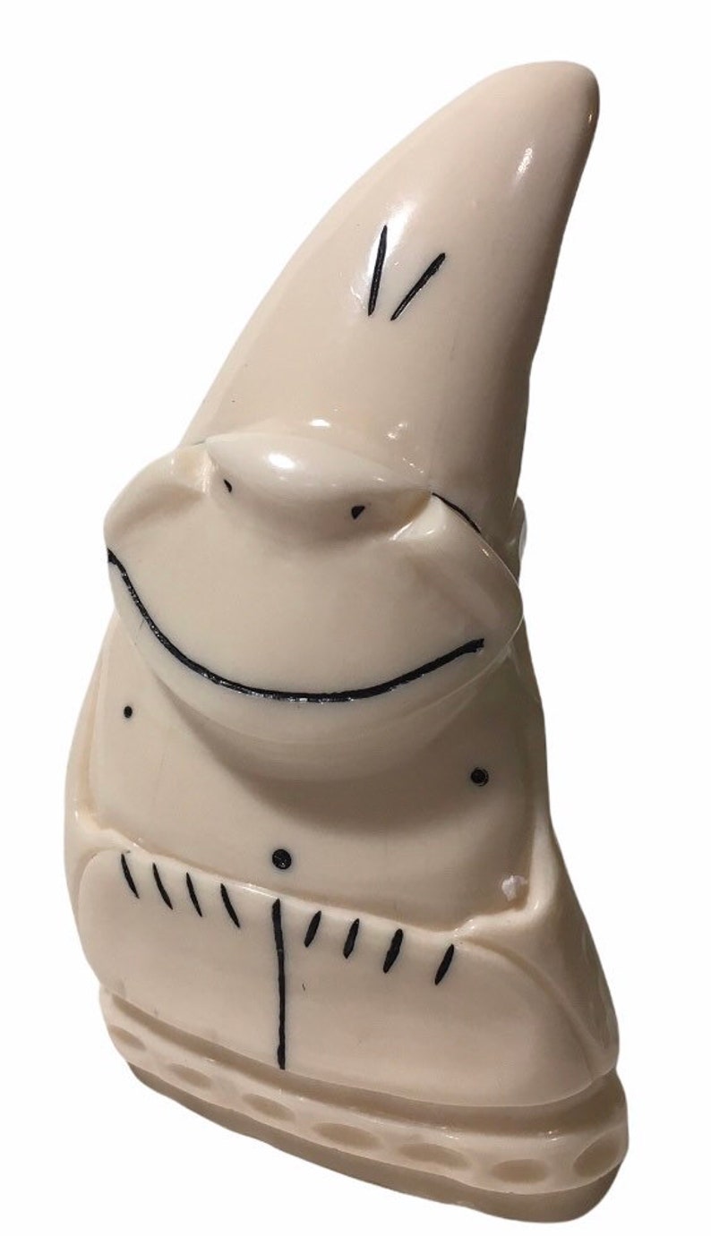 May include: A white ceramic figurine of a smiling gnome with a pointed hat. The gnome is wearing a simple outfit with a few lines of detail.
