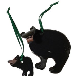 Könnte beinhalten: Zwei schwarze Keramik-Bären-Anhänger mit grünen Schleifen. Der größere Bär steht, der kleinere sitzt. Beide Bären haben braune Nasen und Augen.