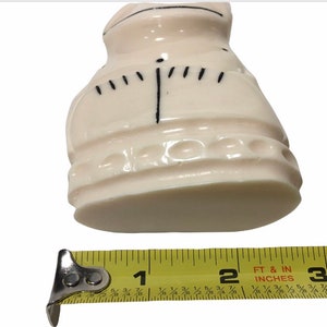 May include: A white ceramic figurine of a person wearing a dress with a black design. The figurine is approximately 2 inches tall.