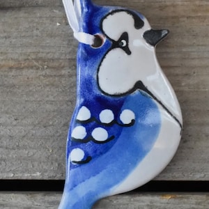 May include: A blue and white ceramic bird ornament with black details. The bird has a white head with black eyes and a blue body with white spots. The ornament is hanging from a white ribbon.