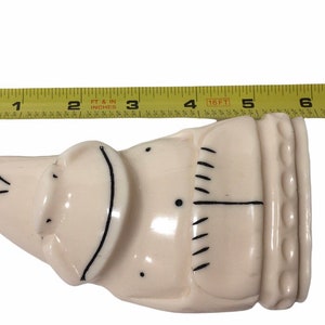 May include: A white ceramic figurine of a person with black line details. The figurine is approximately 5 inches long.
