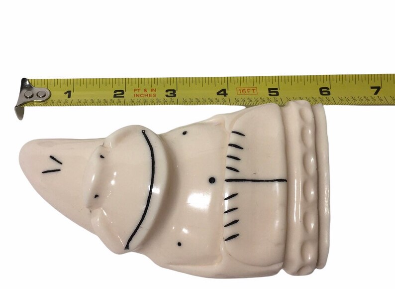 May include: A white ceramic figurine of a person with black line details. The figurine is approximately 5 inches long.