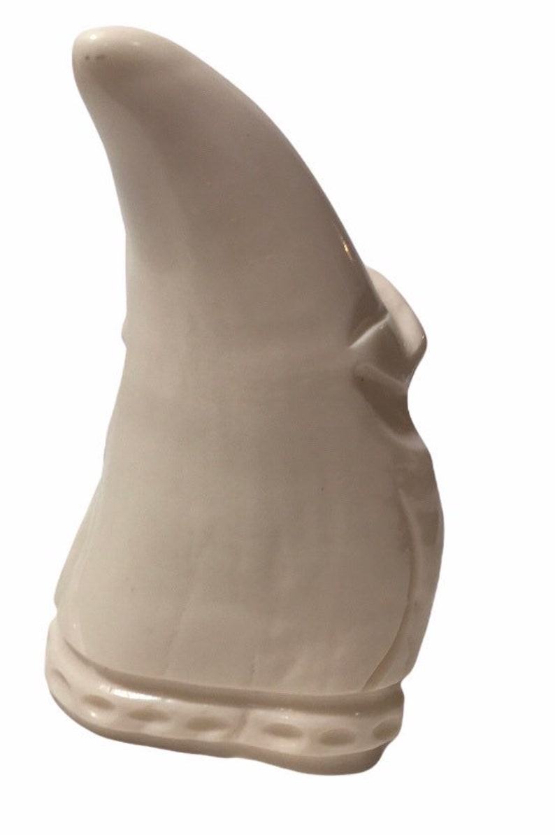 May include: White ceramic figurine of a gnome with a pointed hat. The gnome is wearing a long, flowing robe and has a beard.