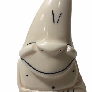 May include: A white ceramic figurine of a smiling gnome with a pointed hat. The gnome has black eyes and a black mouth.