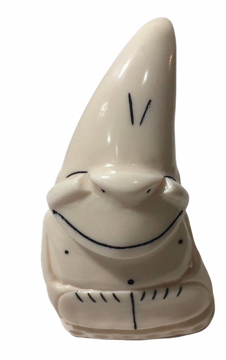 May include: A white ceramic figurine of a smiling gnome with a pointed hat. The gnome has black eyes and a black mouth.