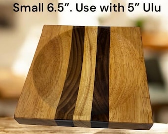 Peut inclure: Une petite planche à découper carrée en bois avec une indentation circulaire. La planche est faite de bandes de bois claires et foncées, avec le texte "Small 6.5". Use with 5" Ulu" en haut. La planche mesure environ 16,5 cm de côté.