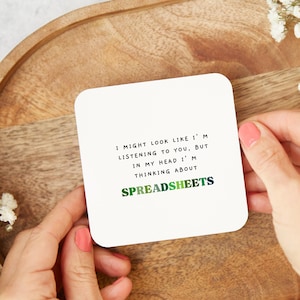 May include: White coaster with the text "I might look like I'm listening to you, but in my head I'm thinking about SPREADSHEETS". The text "SPREADSHEETS" is in green, blue, and black.