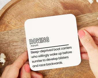 May include: A square white card with rounded corners featuring the black text ROWING, noun, and the definition: Sleep-deprived boat carriers who willingly wake up before sunrise to develop blisters and race backwards.
