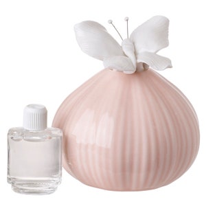 May include: A pink ceramic diffuser with a white porcelain butterfly on top. The diffuser has a ribbed design and comes with a small bottle of essential oil.