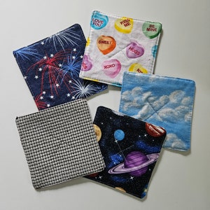 May include: Set of 6 colorful fabric coasters with various designs. The coasters feature a variety of patterns, including fireworks, clouds, hearts, and stars. The coasters are perfect for protecting surfaces from heat and spills.