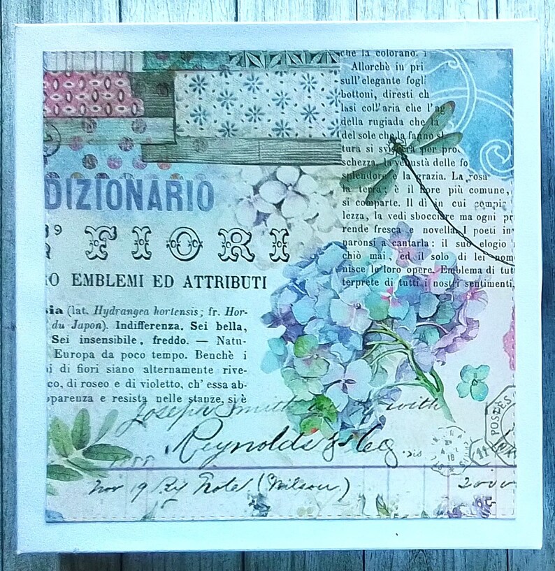 May include: A square canvas wall art piece featuring a collage of vintage-style Italian text, hydrangea flowers in shades of blue and purple, and a dragonfly illustration. The design includes script handwriting, postal stamps, and floral patterns.