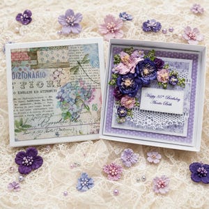 May include: A square greeting card box set featuring a vintage-style floral collage on the left lid and a layered card on the right. The card displays purple and pink fabric flowers, a white lace border, and a label reading Happy 85th Birthday Auntie Beth.