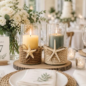 May include: Two cylindrical glass candle holders wrapped in thick rope, each featuring a white starfish accent. One holder contains a cream-colored pillar candle, while the other holds a sage green pillar candle, both resting on a wood slice.