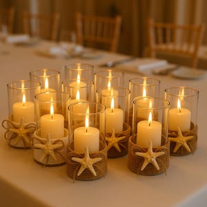May include: A collection of clear glass cylinder candle holders, each wrapped at the base with natural tan jute twine and adorned with a single cream-colored starfish. Each holder contains a lit white pillar candle, creating a warm glow.