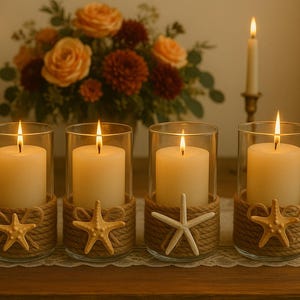 May include: Four cylindrical glass candle holders, each containing a white pillar candle. The base of every glass is wrapped in thick tan rope, decorated with a small, light-colored starfish figure. Two tall taper candles stand in the background.