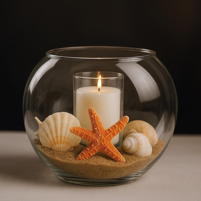 May include: A clear glass bowl with sand, seashells, and an orange starfish. A white candle in a glass holder is lit inside the bowl. The candle flame is bright against the dark background.