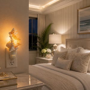 May include: A wall plug-in night light featuring a textured, off-white seashell design that emits a warm, golden glow. The light is plugged into a standard electrical outlet on a wall, providing soft illumination to the surrounding area.
