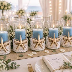 May include: Five cylindrical glass candle holders, each containing a light blue pillar candle. The base of every glass holder is wrapped in thick white rope and decorated with a single beige starfish tied with thin twine.
