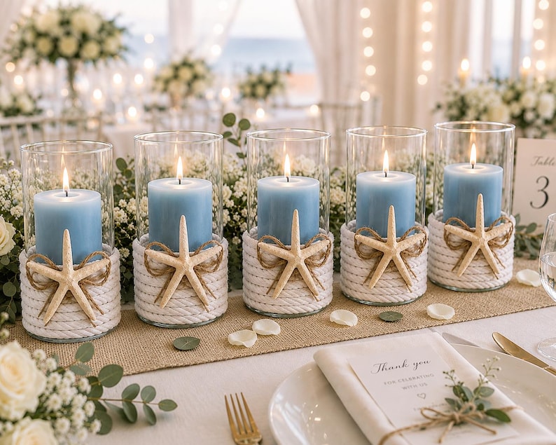May include: Five cylindrical glass candle holders, each containing a light blue pillar candle. The base of every glass holder is wrapped in thick white rope and decorated with a single beige starfish tied with thin twine.