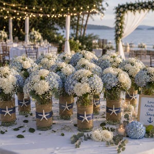 May include: A collection of glass vases filled with blue and white hydrangea bouquets, wrapped in burlap and navy blue ribbon with a white starfish accent. A framed sign reads, Love Anchors the Soul, next to loose white roses and blue hydrangea.