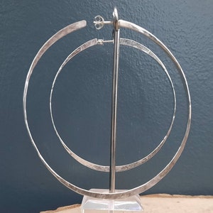 May include: Silver hoop earrings with a hammered finish. The earrings are double layered and have a simple design.