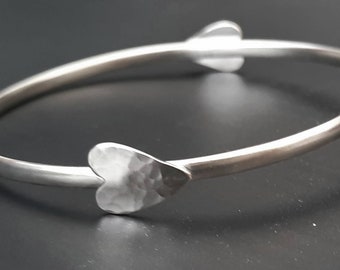 An oval silver bangle with a hammered heart at opposing sides.