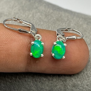 Puede incluir: Un par de pendientes de plata con cierre de palanca, con ópalos ovalados de color verde vibrante y destellos de color. Cada piedra está sujeta de forma segura en un engaste de cuatro garras, unido a un aro de plata pulida para un cierre firme.