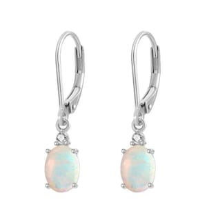 May include: A pair of silver leverback earrings featuring oval-shaped opals set in four-prong settings. Each earring has a small, clear, round-cut accent stone positioned directly above the opal, suspended from a polished silver hook mechanism.
