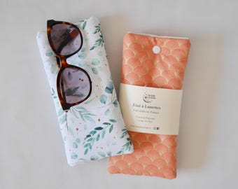 May include: Two eyeglass cases, one with a white background and a green leafy pattern, and the other with a peach background and a gold geometric pattern. The case with the leafy pattern has a pair of brown sunglasses inside. The case with the geometric pattern has a white button closure. Both cases have a label that reads "Etui à Lunettes Fait main en France".