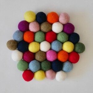 Può includere: Una disposizione colorata di palline di feltro in varie tonalità di rosso, arancione, giallo, verde, blu, viola, rosa e bianco. Le palline sono disposte in un motivo circolare, creando un design visivamente accattivante e testurizzato.
