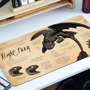 Könnte beinhalten: Rechteckiges Mauspad mit einer schwarzen Drachenillustration und dem Text "Night Fury". Das Design enthält Diagramme und Text über den Drachen auf beigem Hintergrund. Das Pad liegt auf einem weißen Schreibtisch.