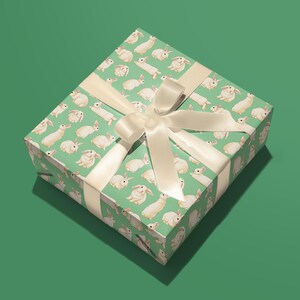 Pu&ograve; includere: Una scatola regalo verde con un nastro bianco e un motivo di conigli bianchi.