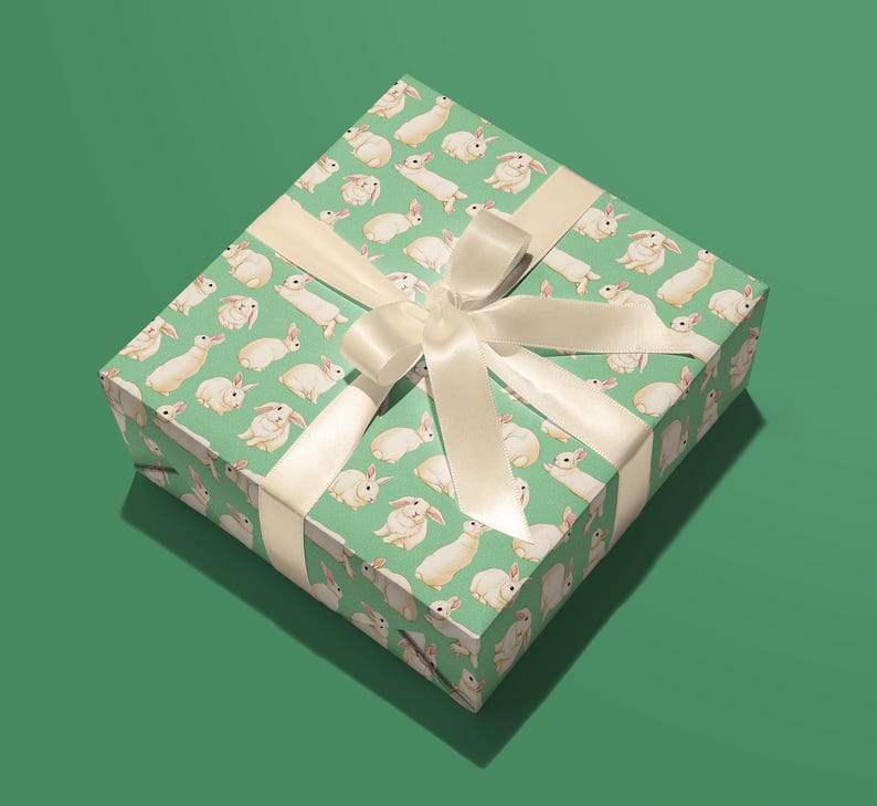 Pu&ograve; includere: Una scatola regalo verde con un nastro bianco e un motivo di conigli bianchi.