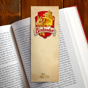 May include: A brown bookmark with a red and gold shield featuring a cartoon bunny rabbit. The shield has the text "Binkindor" in gold lettering. The bookmark is made of paper and has a distressed look. The text "FIRLEFANZ" is printed in the bottom right corner.